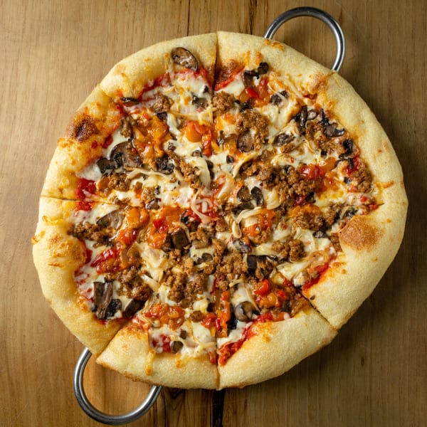 A sliced Italian pizza with sausage, mushrooms, onions, and bell peppers on a wooden table.
