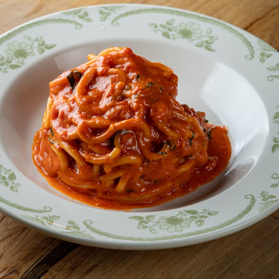Spaghetti with a rich red sauce and herbs, served on a white plate with a green floral rim.