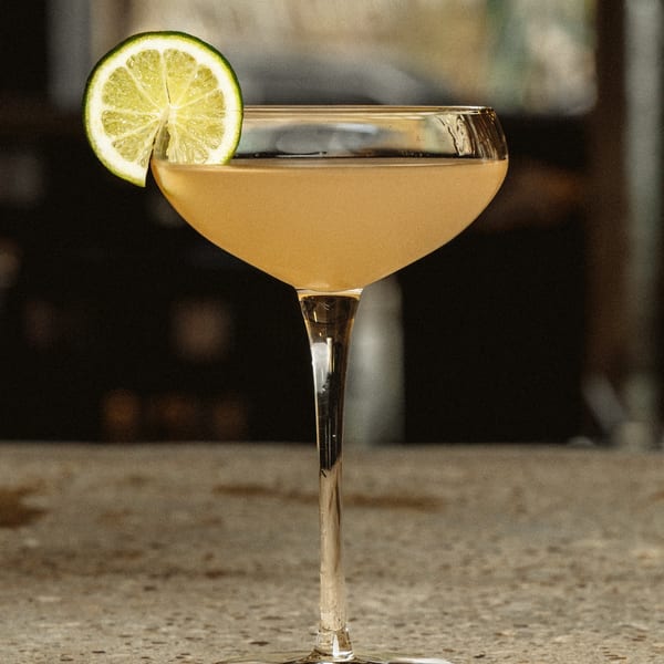 A golden cocktail in a coupe glass, garnished with a fresh lime slice, at Earl & Isabella's Taverna.