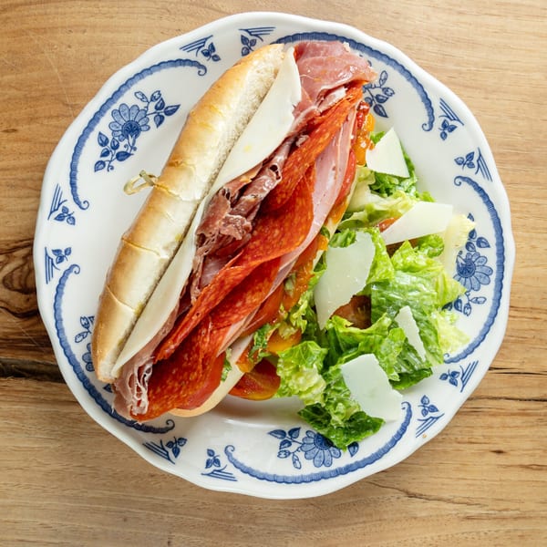 An Italian sub sandwich with salami, pepperoni, and cheese, served with a side salad.