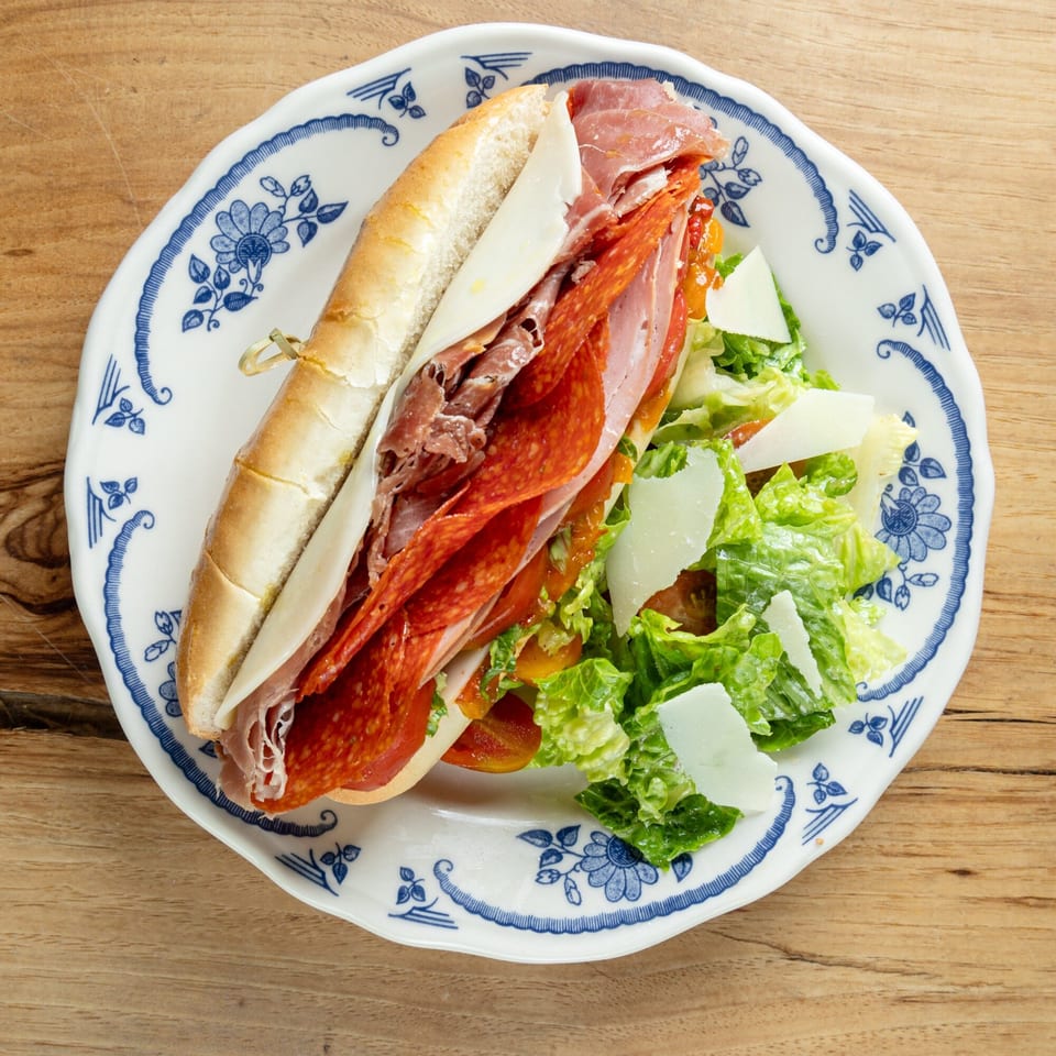 An Italian sub sandwich with salami, pepperoni, and cheese, served with a side salad.