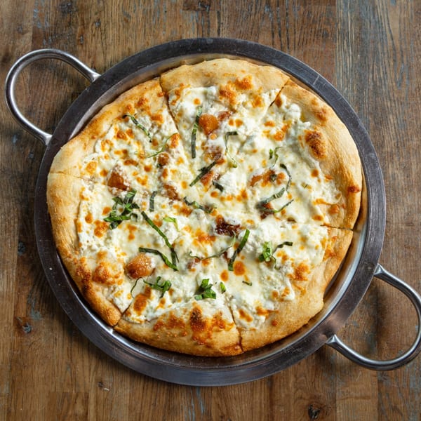 A white pizza with ricotta cheese, mozzarella, and basil on a metal pan at Earl & Isabella's Taverna.