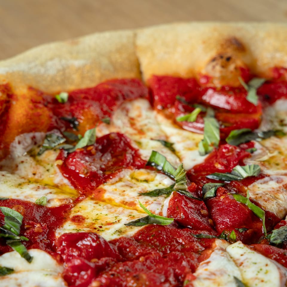 Close-up of a freshly baked Earl & Isabella's Taverna pizza with rich red sauce, mozzarella, and basil.