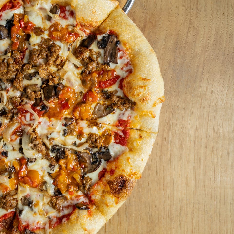 Close-up of a half-eaten Italian pizza with sausage, mushrooms, onions, and peppers on a wooden table.