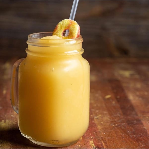 Mason jar filled with a yellow frozen drink, garnished with a peach ring and a straw.