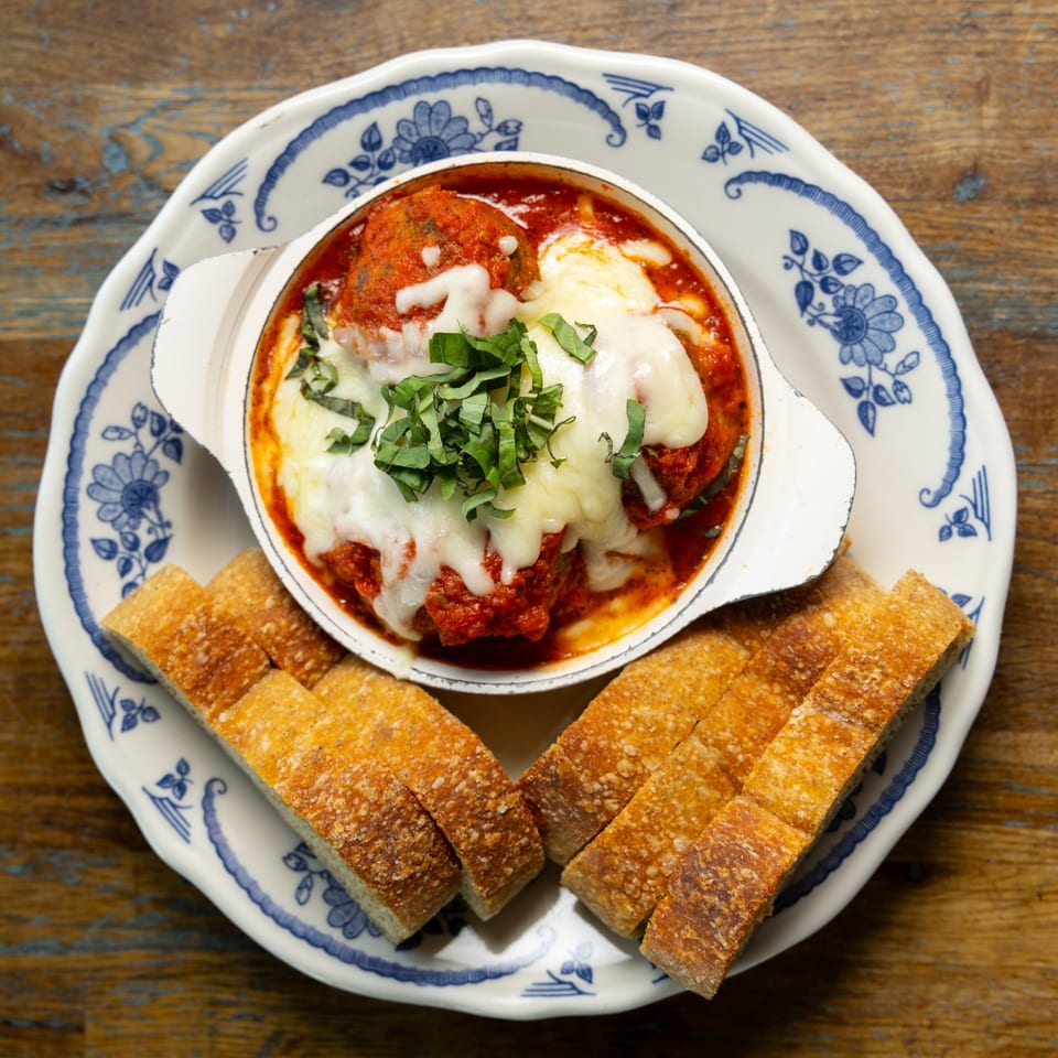 Italian meatballs baked in marinara sauce with melted mozzarella and fresh basil, served with sliced bread.