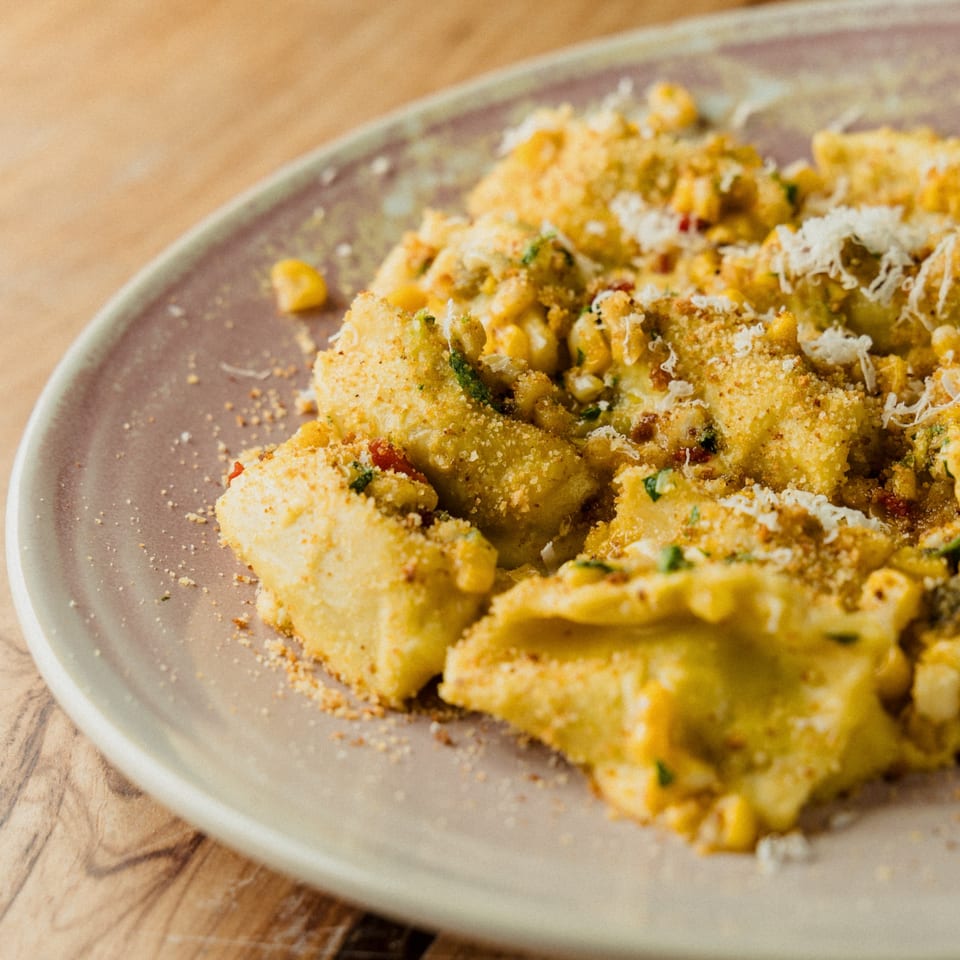 Close-up of Earl & Isabella's Taverna's ravioli dish, topped with corn, breadcrumbs, and grated cheese.